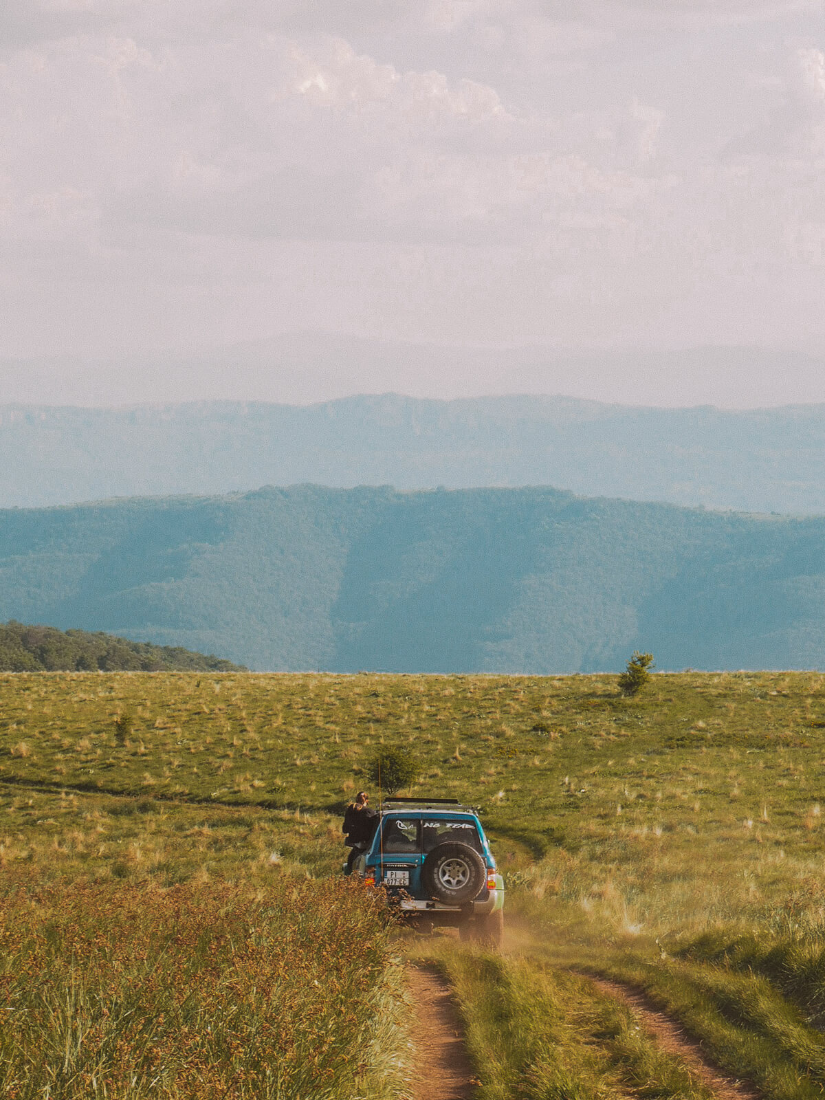 Ein Jeep fährt durch eine Bergwiese, im Hintergrund blaue Berge