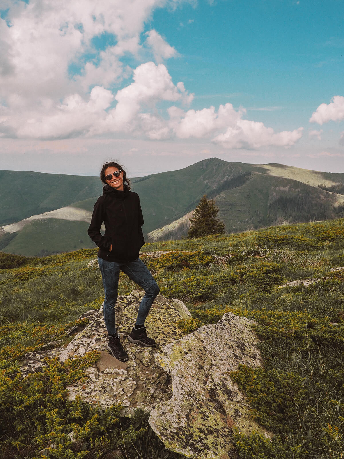 Eine Frau steht auf einem Felsen, im Hintergrund ein grünes Bergpanorama